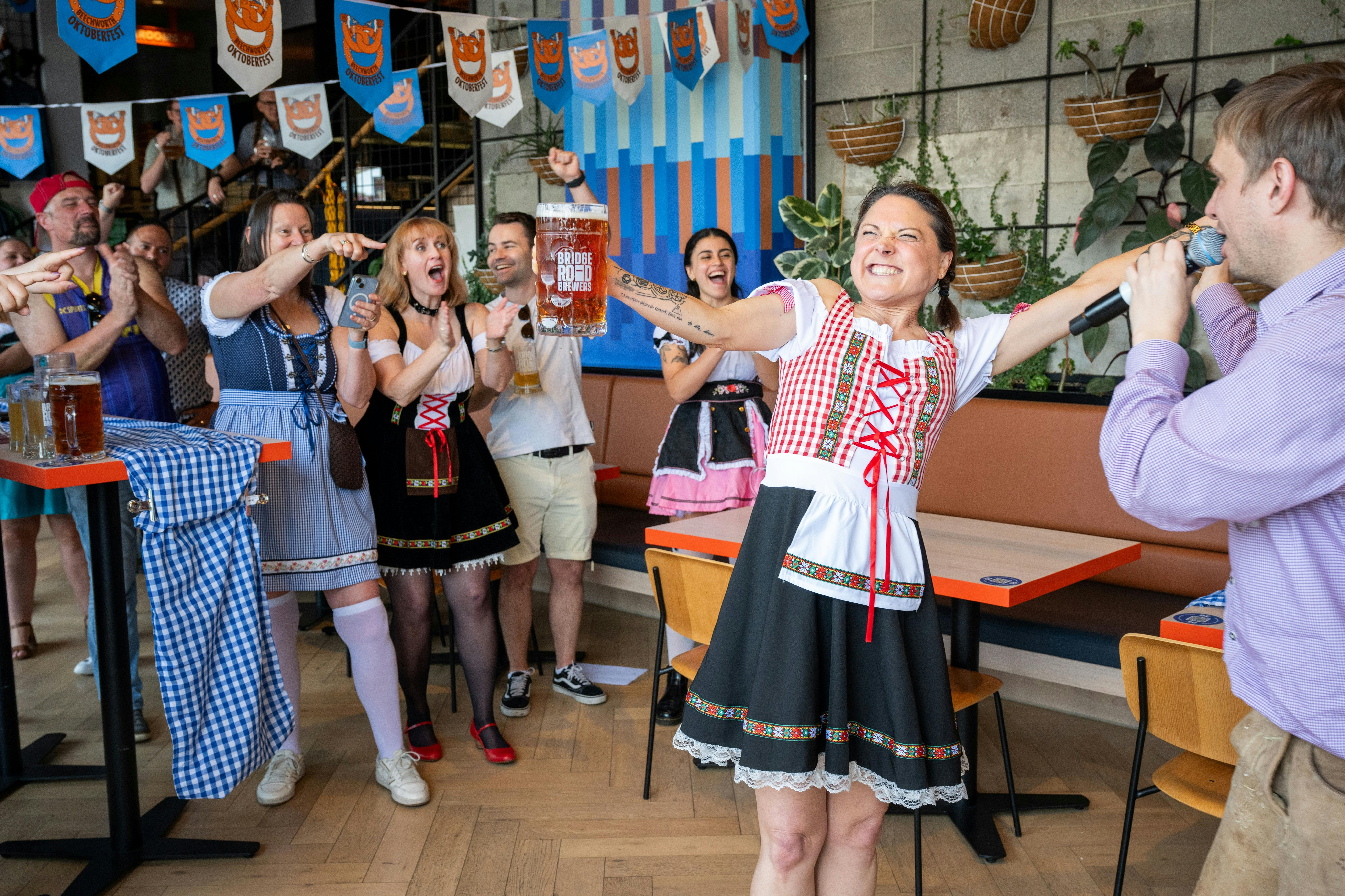 Woman smiling while raising glass in the air and people cheering around her.