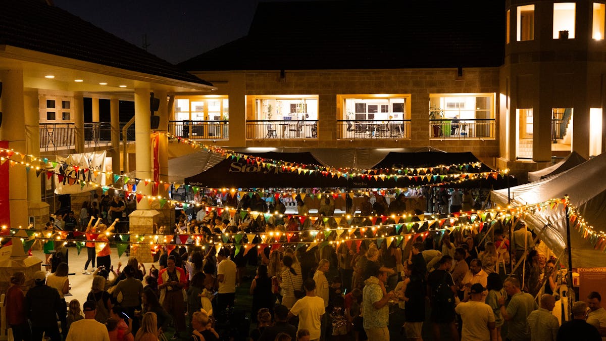 Crowds gathering at a lively outdoor night festival with string lights and market tents