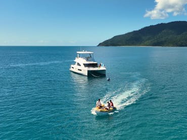 Three people riding in a dinghy in front of a catamaran Three people riding in a dinghy in front of a catamaran