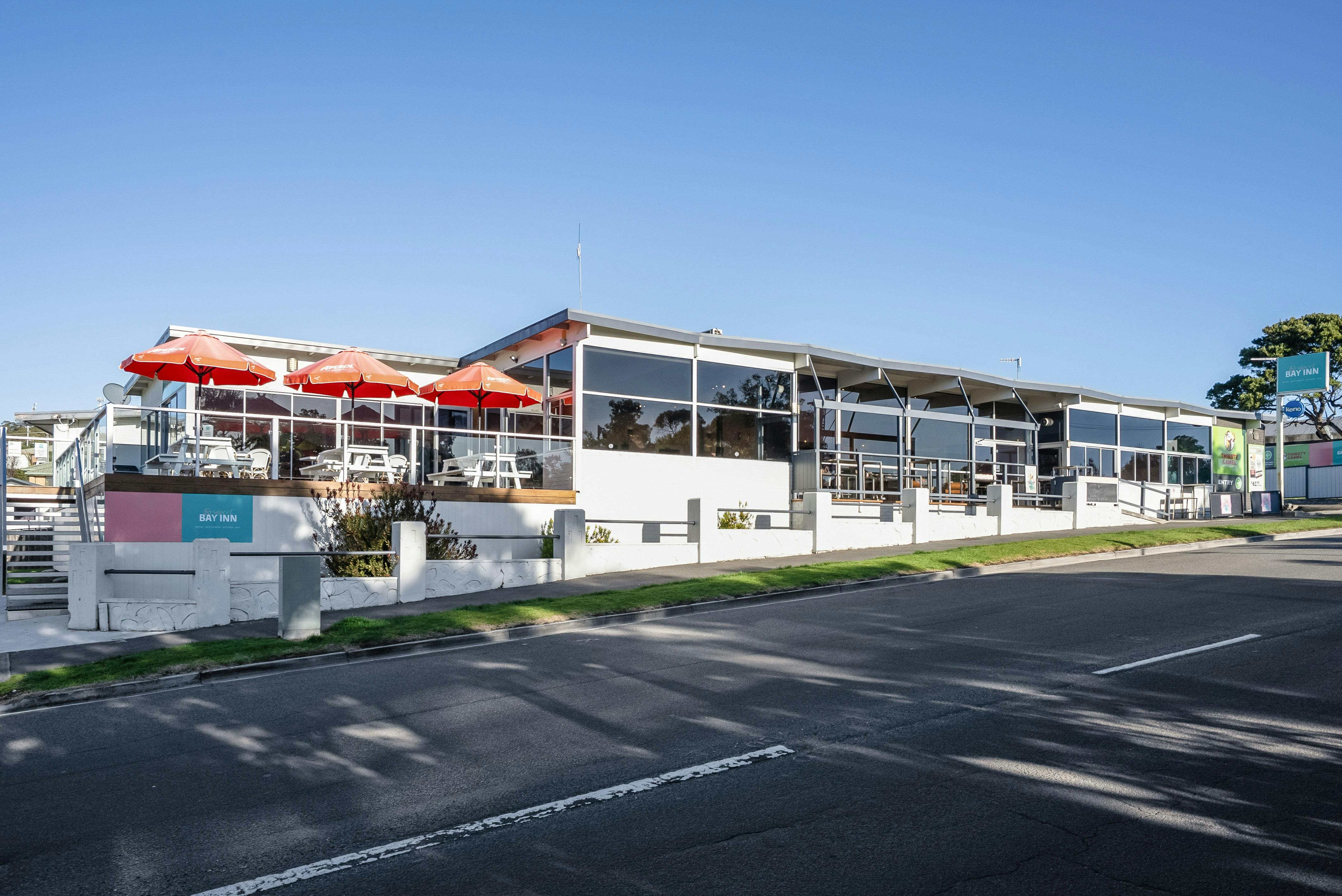 Exterior view of Bridport Bay Inn in Bridport, Tasmania, featuring outdoor deck seating with red umb