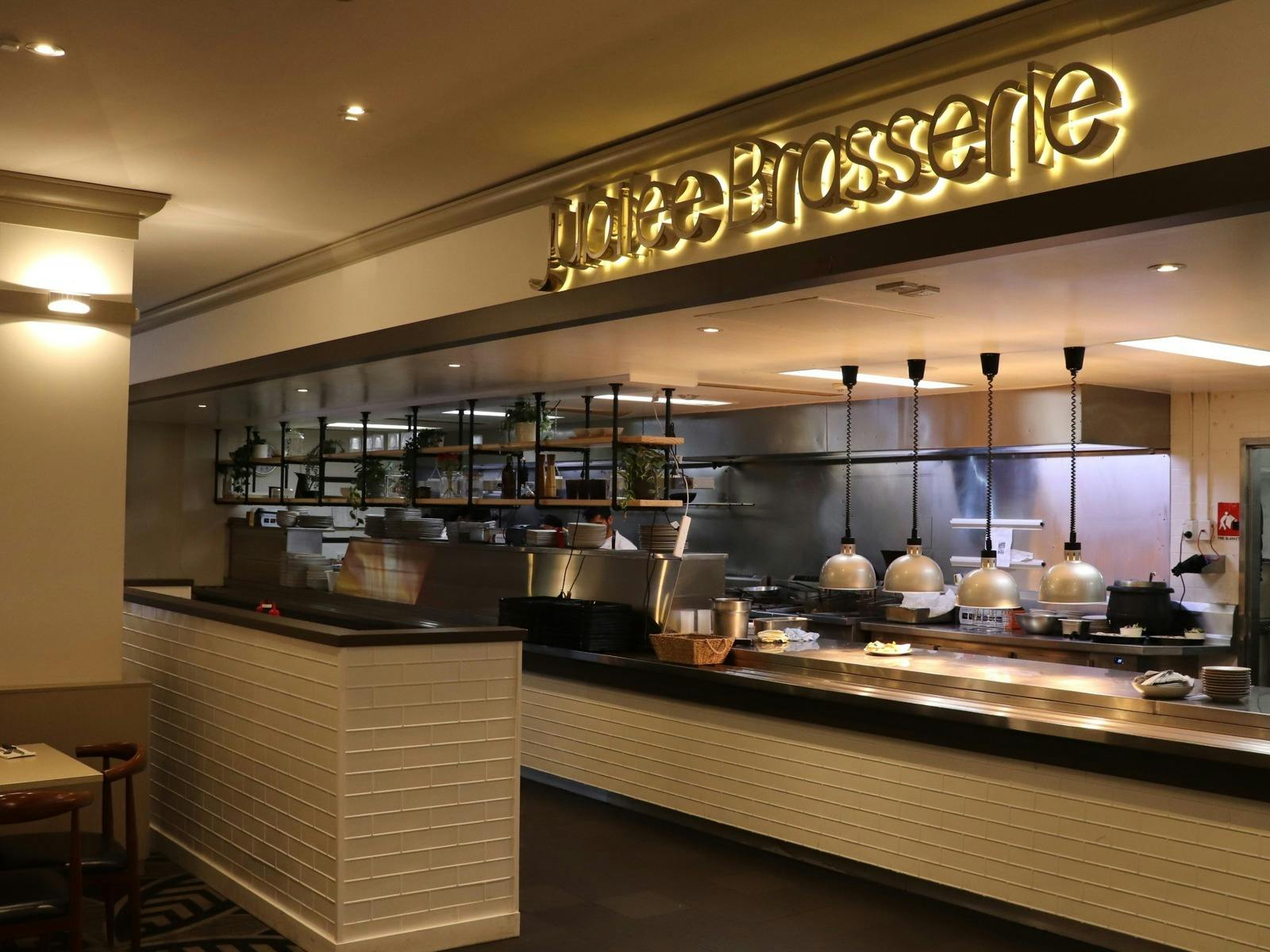 A well-lit kitchen area under a sign reading "Jubilee Brasserie".
