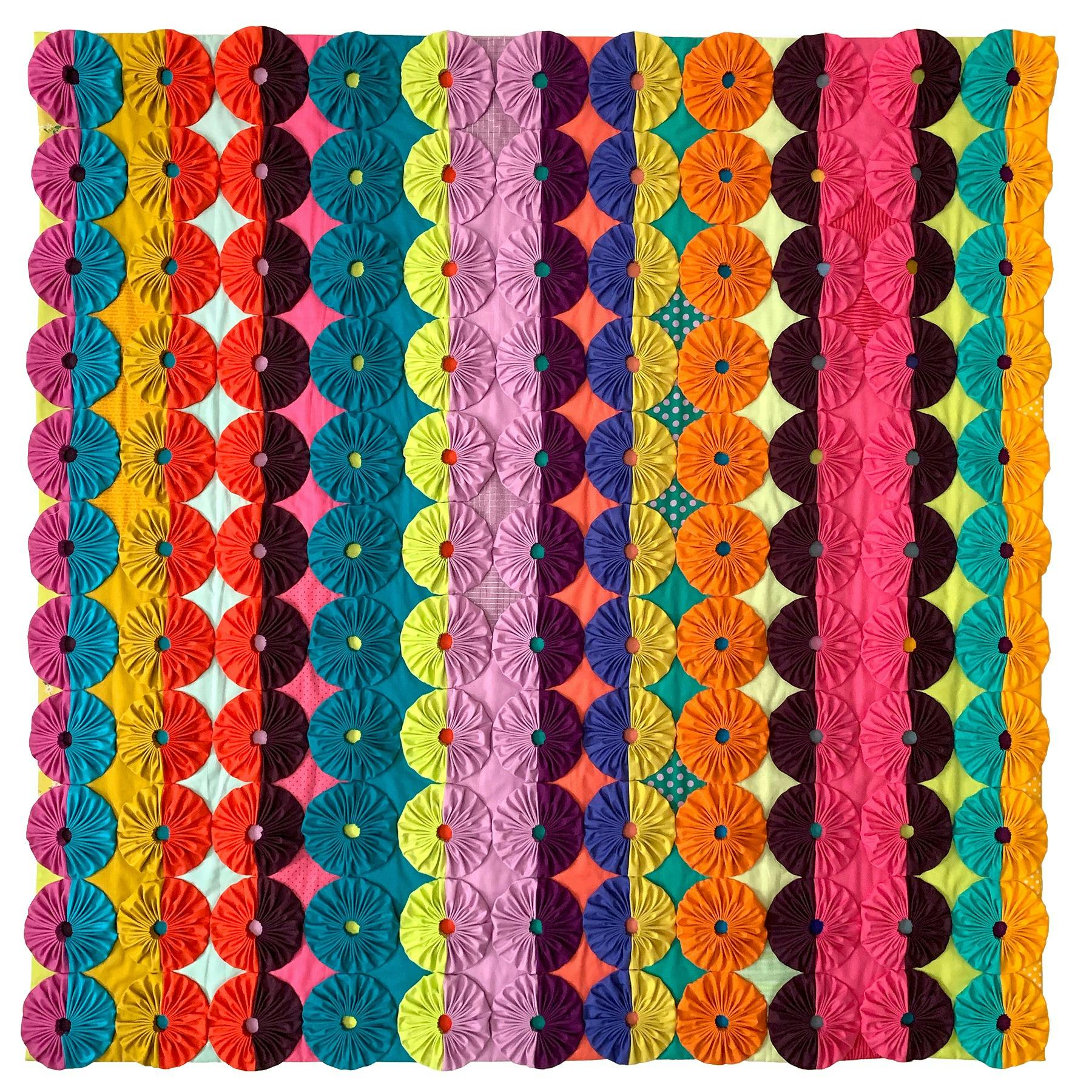 A colourful quilt made up of circular, abstract fabric flowers