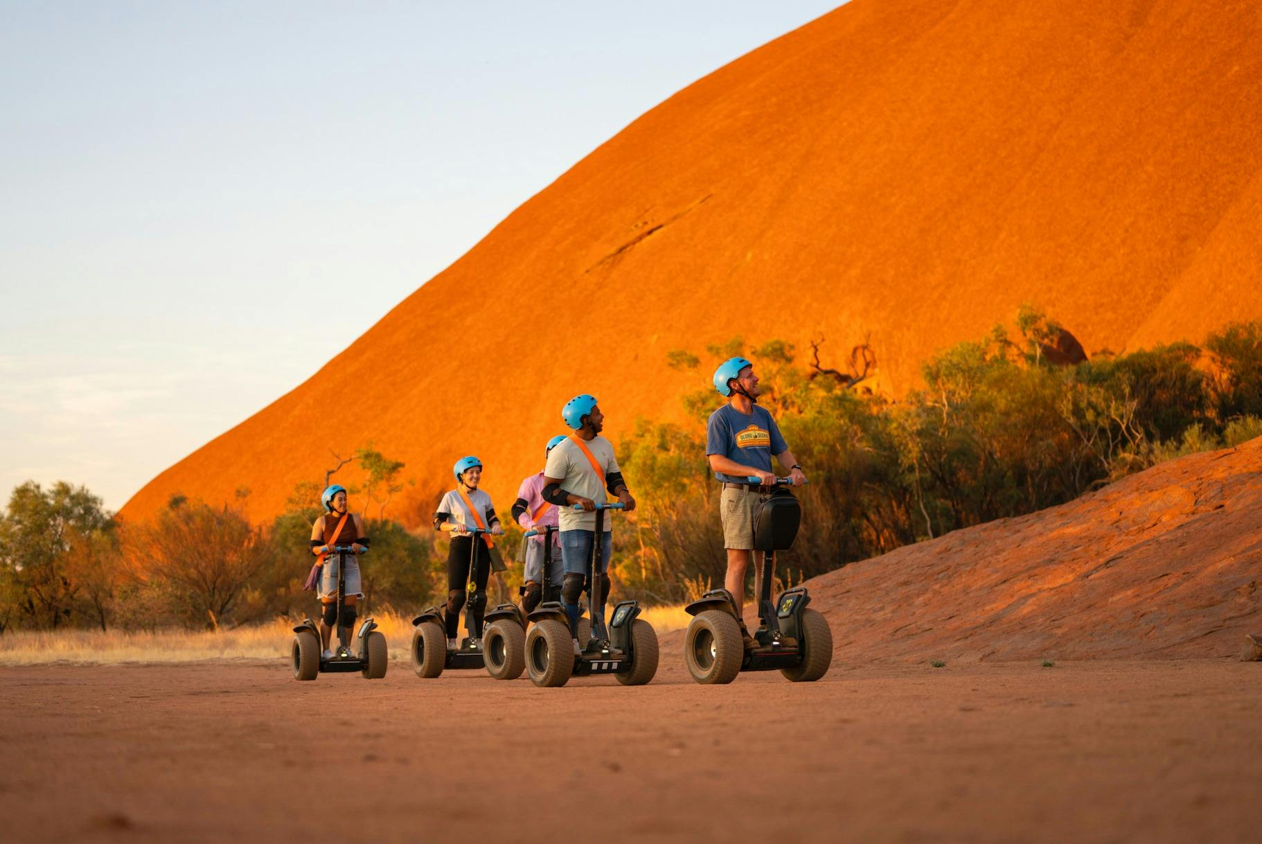 A Segway tour ride towards the camera, with Uluru glowing a bright orange behind them