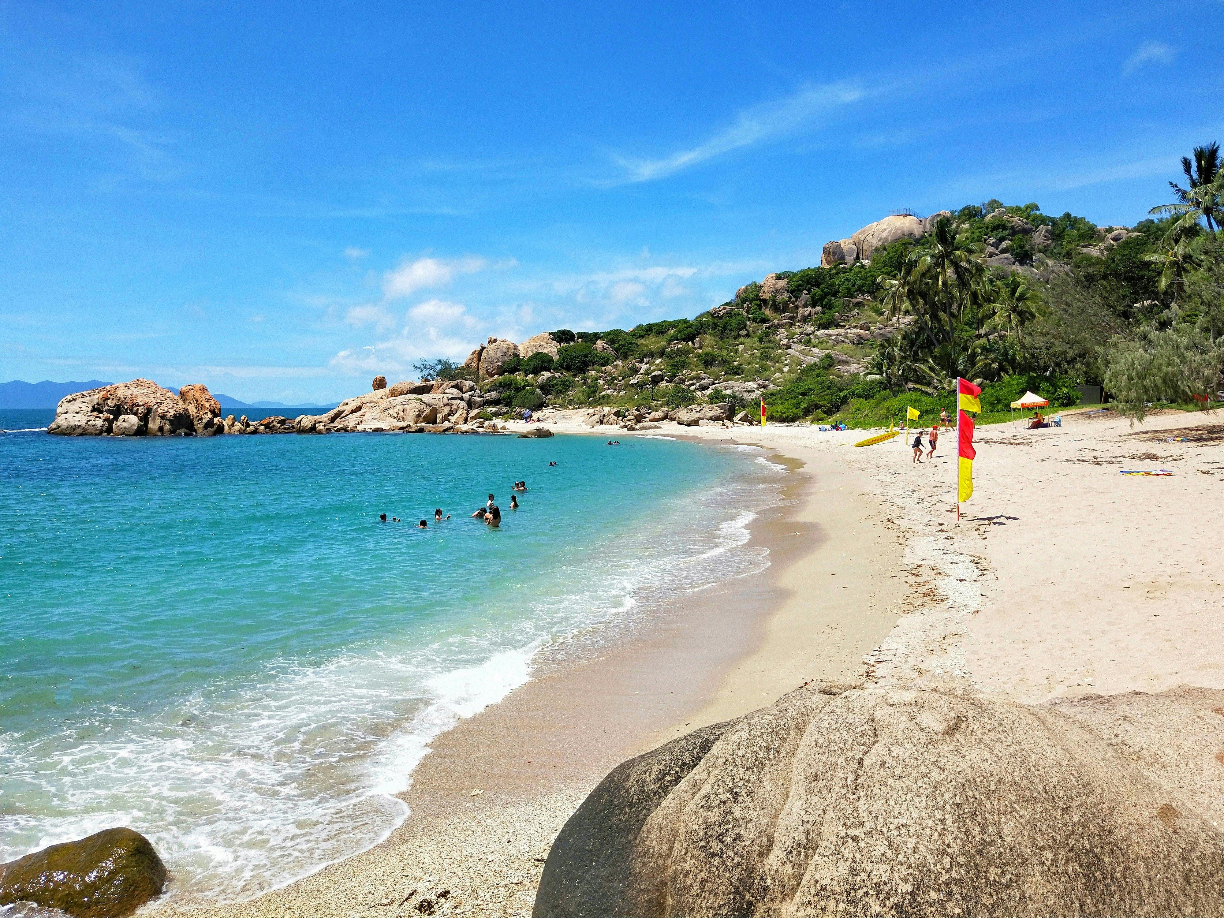 People swimming and life guard on sandy beach in protected bay