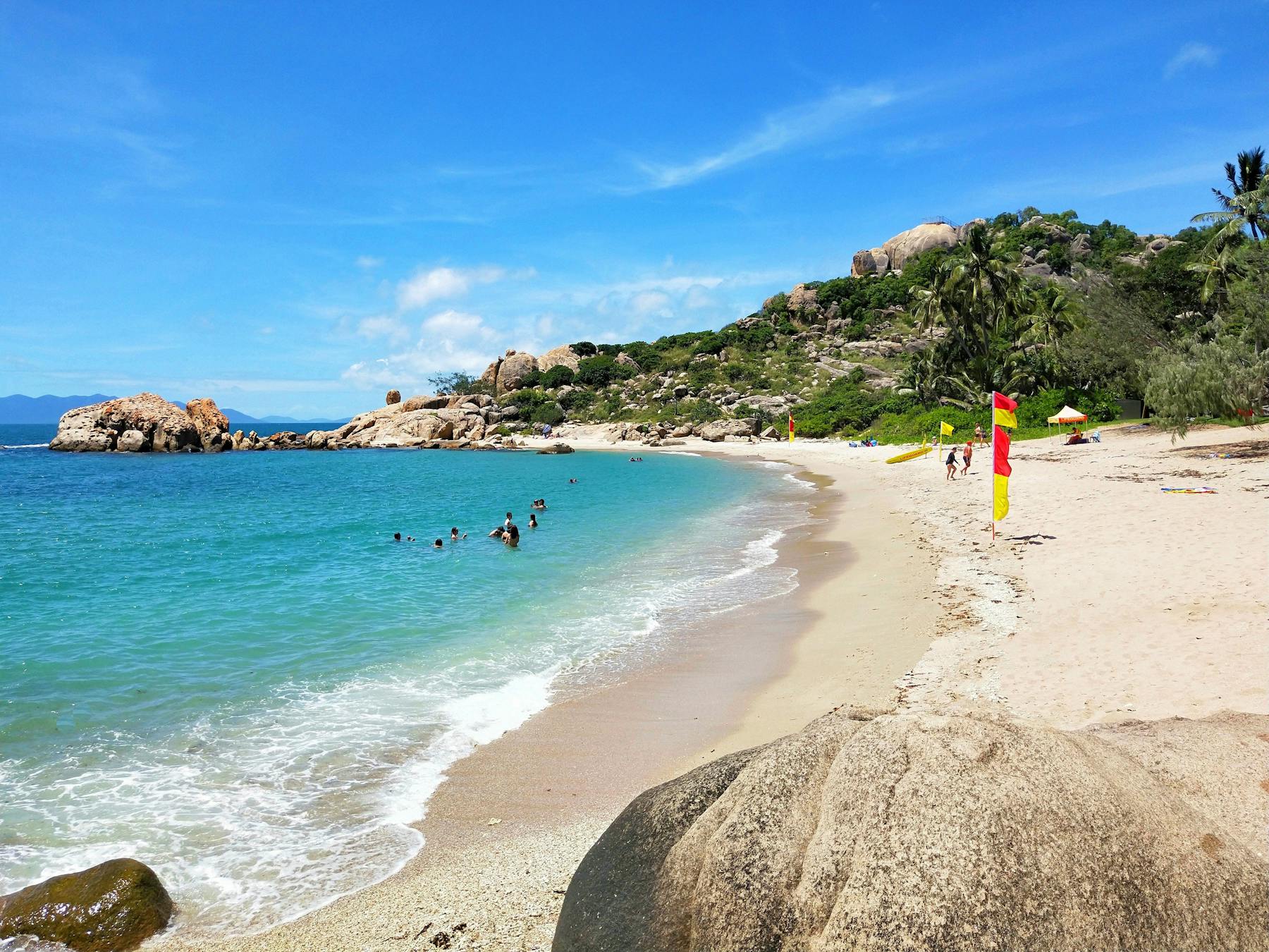 People swimming and life guard on sandy beach in protected bay