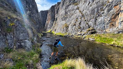 A hiker hopping across rocks to cross a river in a gorge.