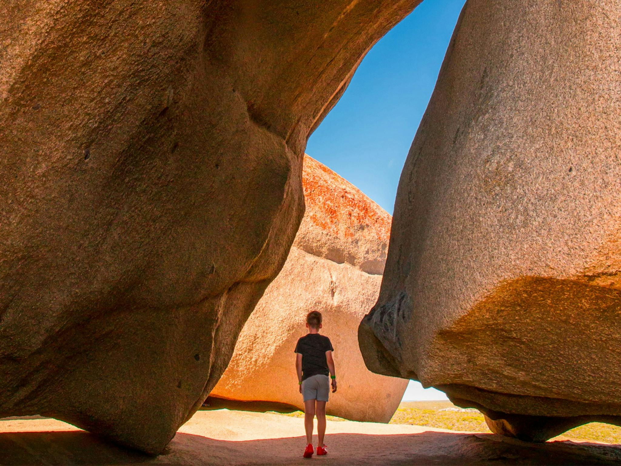 A young boy stands between two rocks
