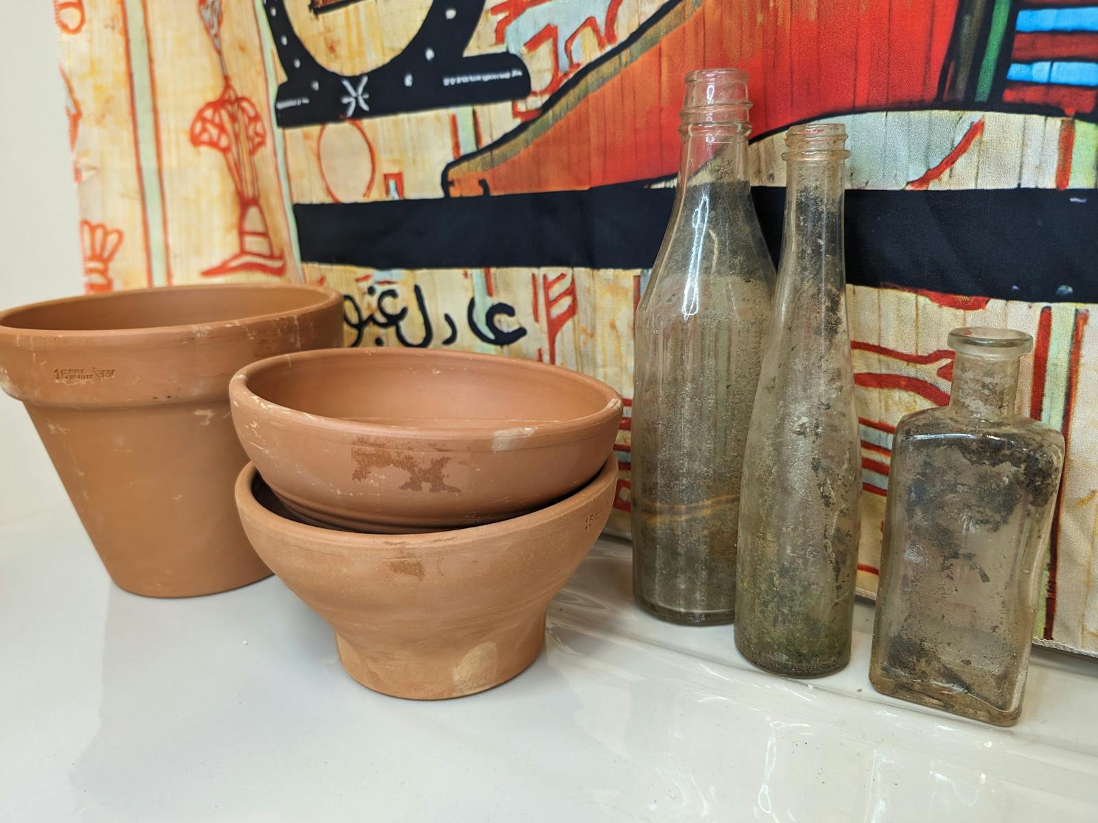 A collection of terracotta pots and weathered bottles against an Egyptian hieroglyph backdrop, sugge