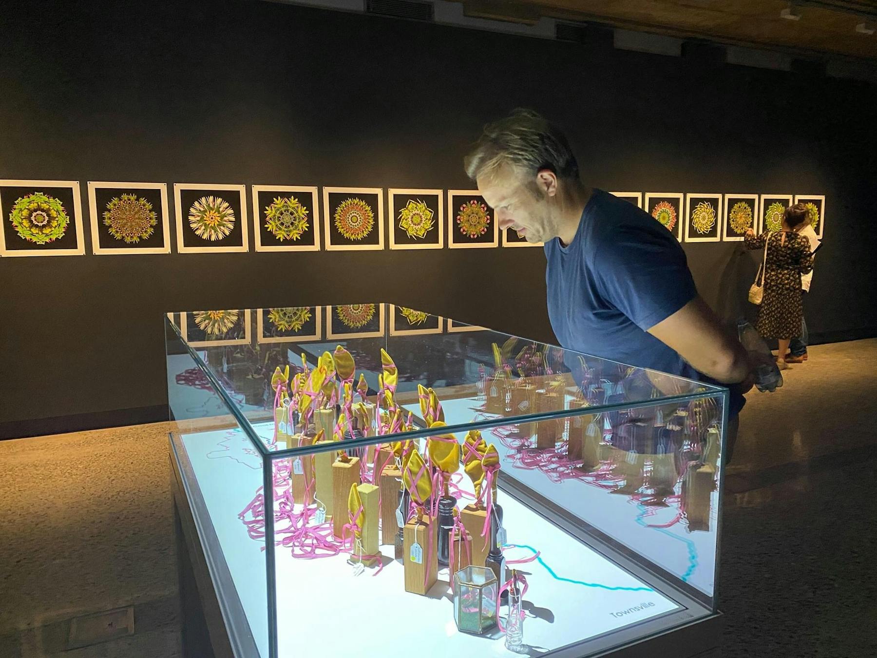 A man looks at a vitrine containing contemporary art sculptures in a darkened gallery with prinrs