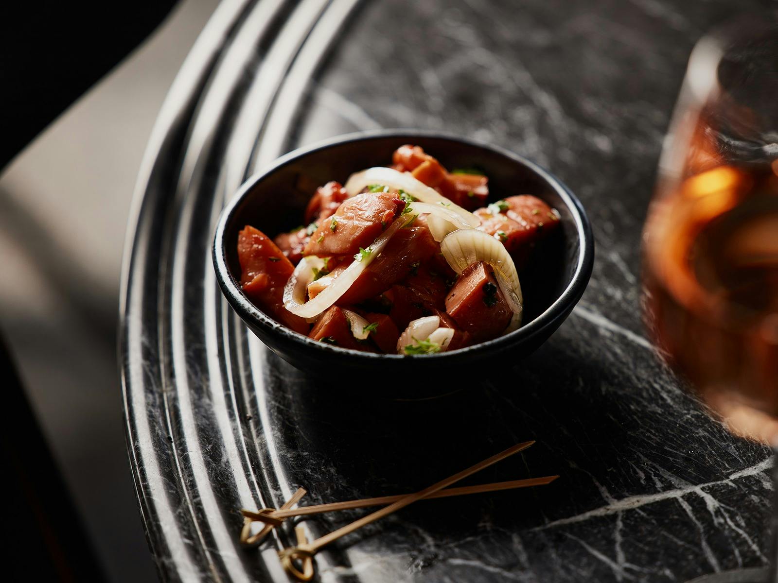 Bowl of pickled octopus on a dark table, sitting next to a glass of wine.