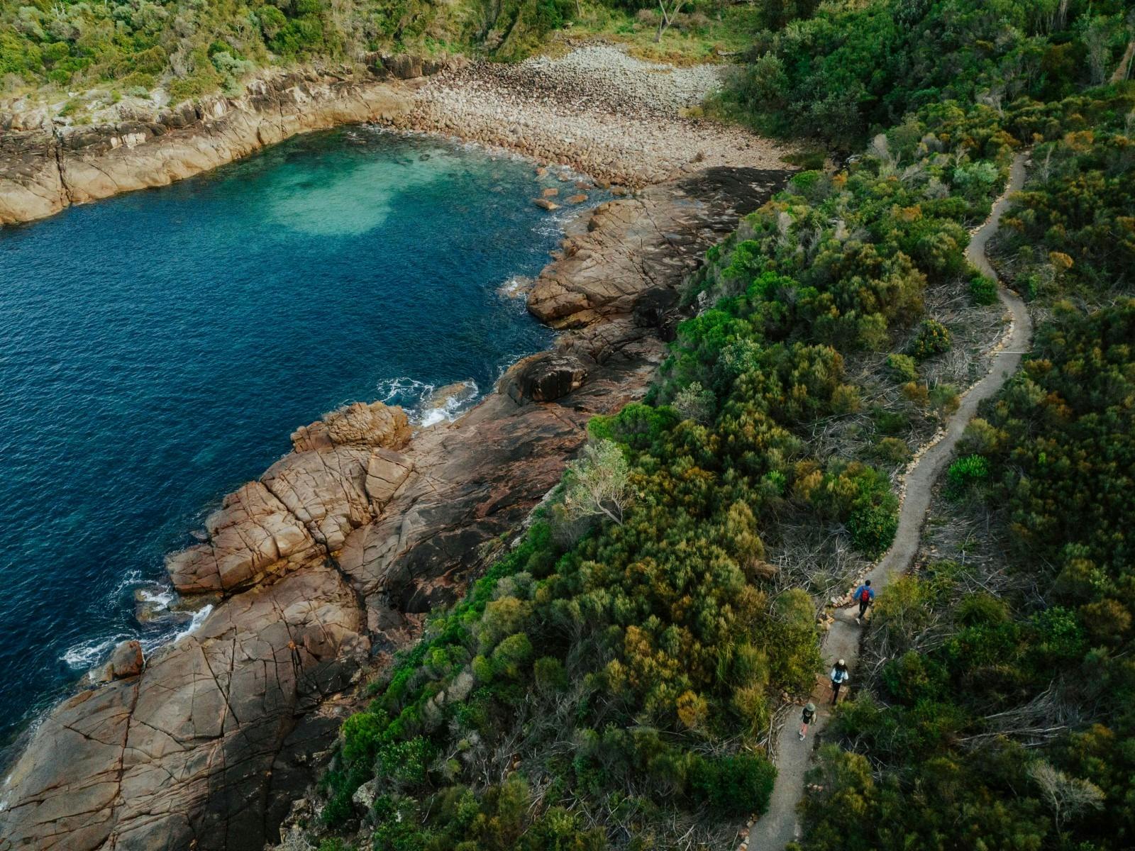 An aerial view with 3 people walking on a track next to a blue cove