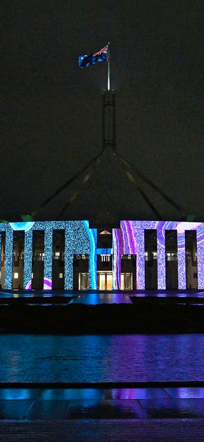 Parliament House at night time with the front facade lit up with the Honey Ant artwork.