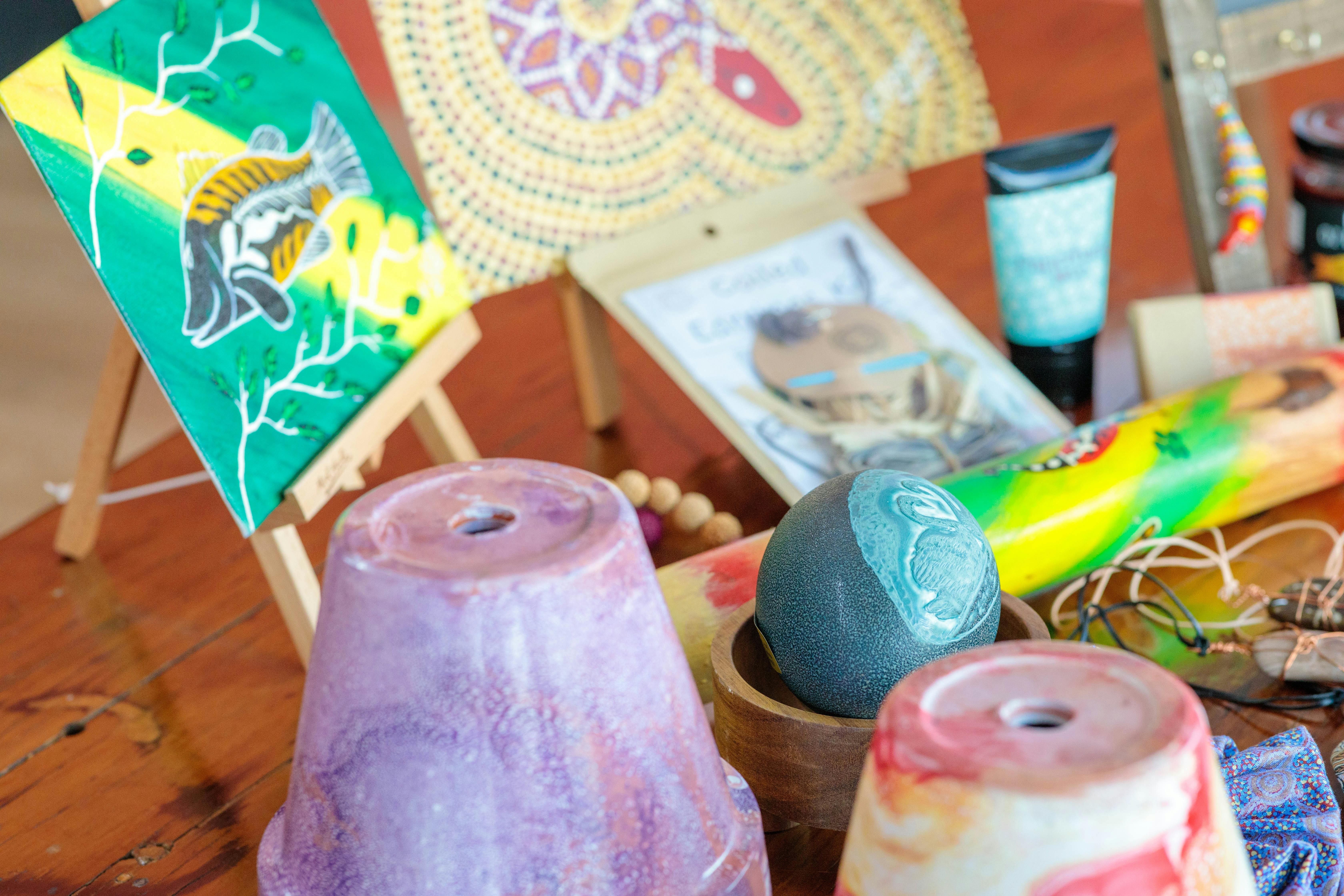 Picture shows artwork of fish and snake, coloured pots, carved emu egg, painted didgeridoo