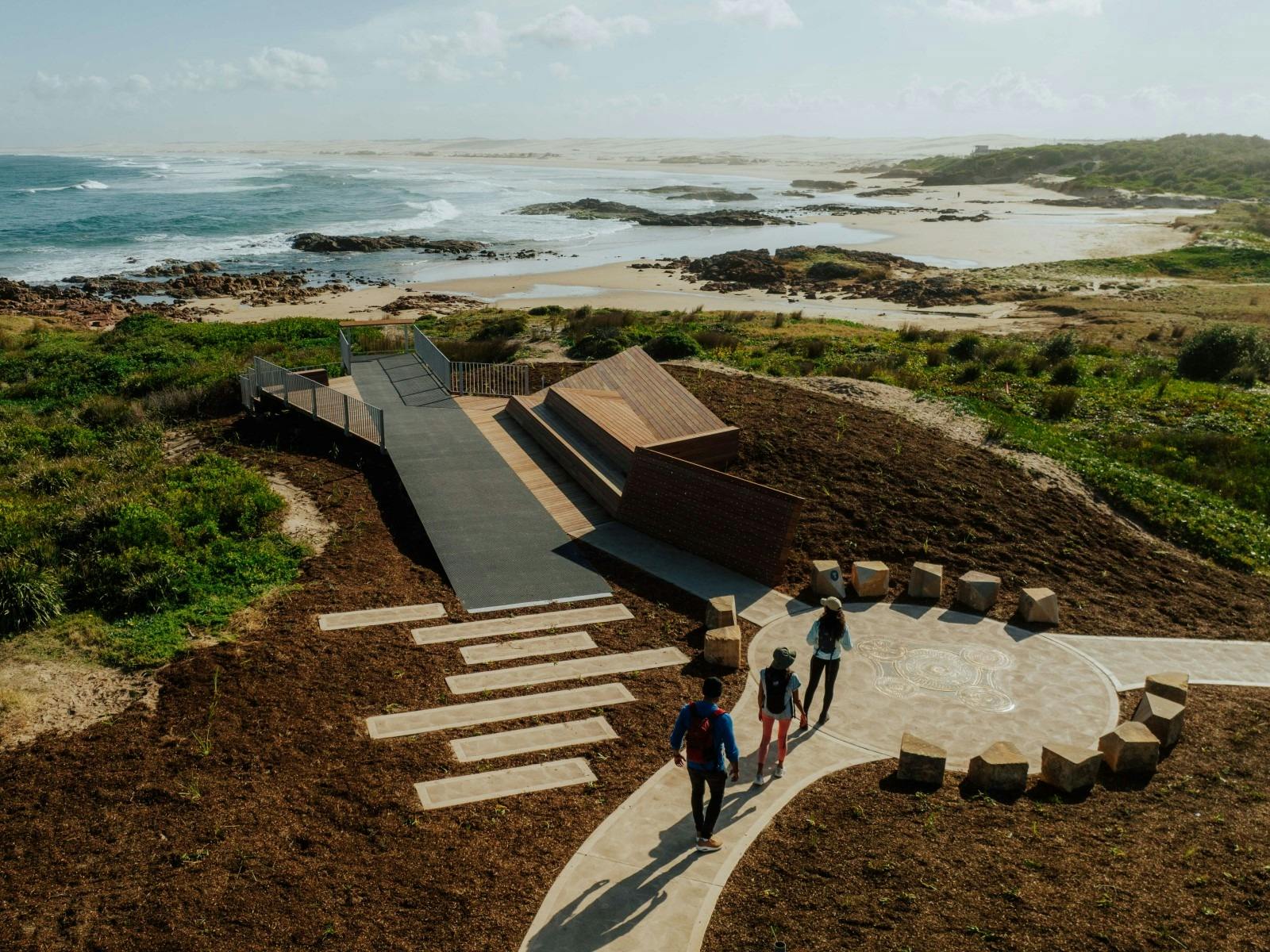 A group of people at the art installation at Birubi Point Aboriginal Place, with ocean in background