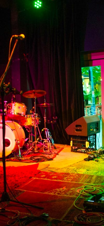 Image of a drumset, microphone, a couple of amps on a stage with red and green lighting.