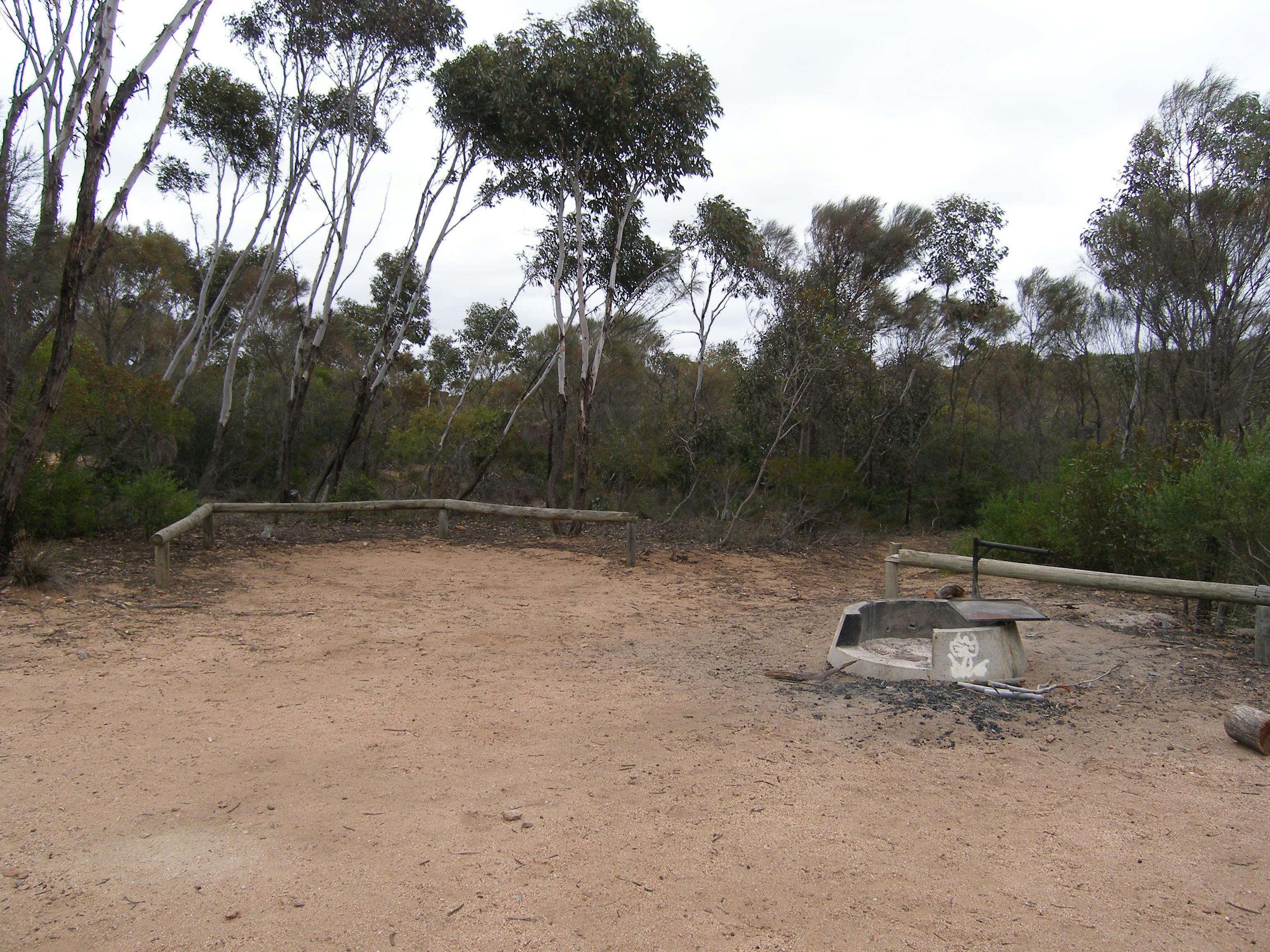 Cleared area surrounded by woodern bollards. There is a concrete fire pit.