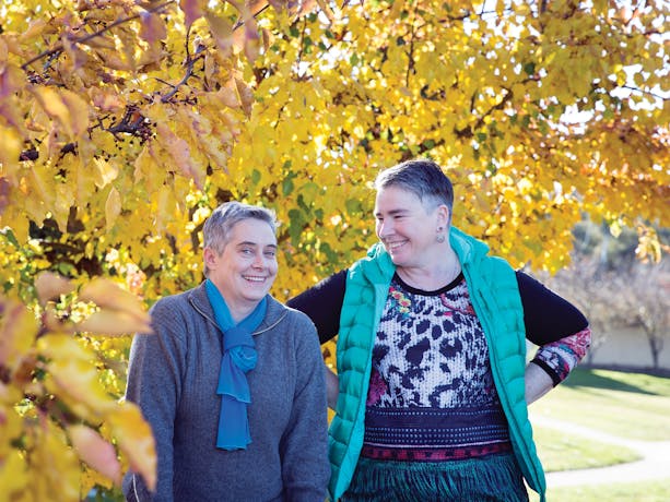 Two women standing happily under a tree with yellow leaves during Autumn in Canberra