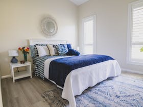 Bedroom with bed covered with qhite coverlet and blue throw rug