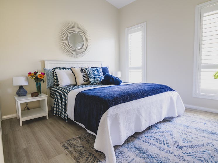 Bedroom with bed covered with qhite coverlet and blue throw rug