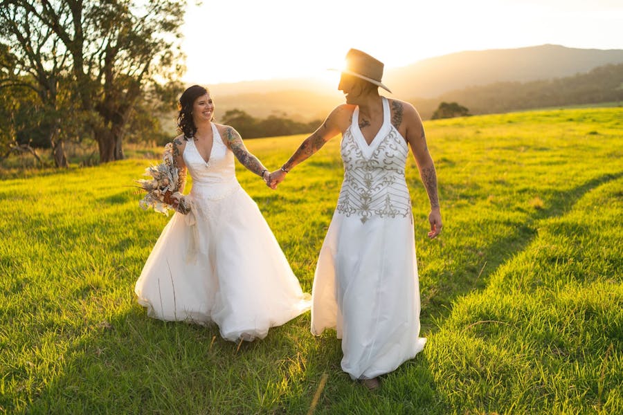 Two brides walk through a field at golden hour