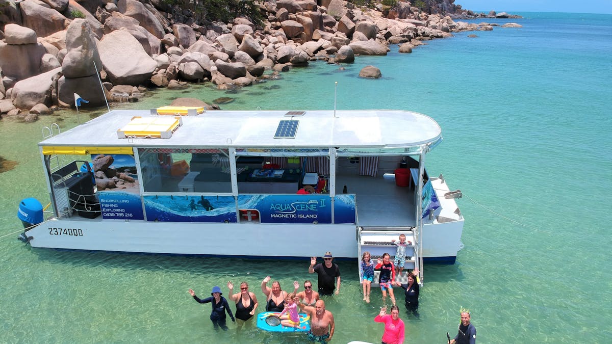 boat near edge of beach in blue clear shallow water with people waving and standing in water smiling