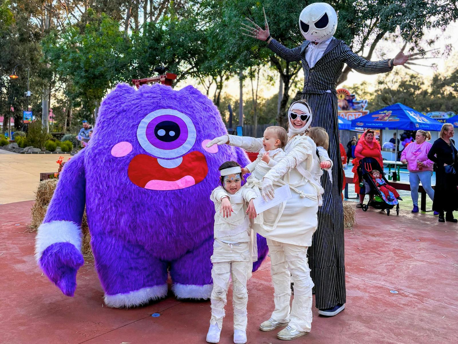 One adult and two children dressed up as mummies with Jack Skeleton and purple monster characters.