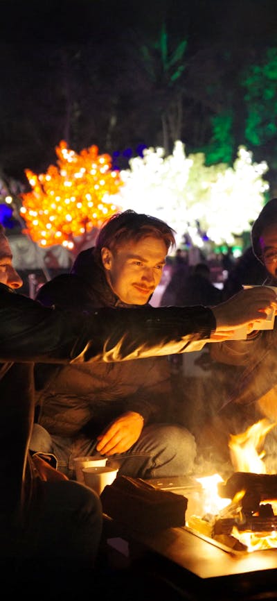 Group of friends cheering with mulled wine around fire pit
