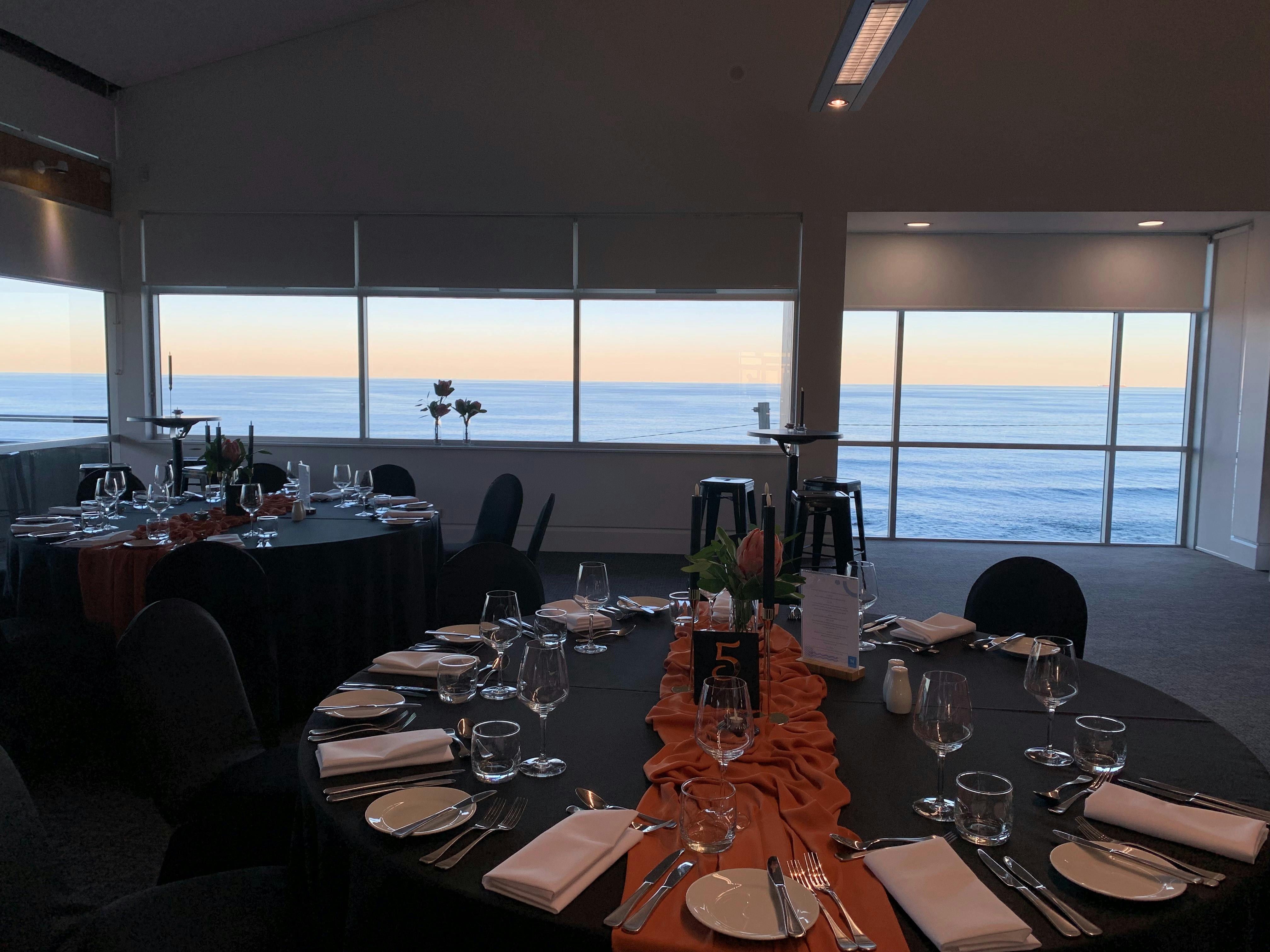 Inside Fort Scratchley Function Centre with tables set for dinner. The ocean can be seen outside.
