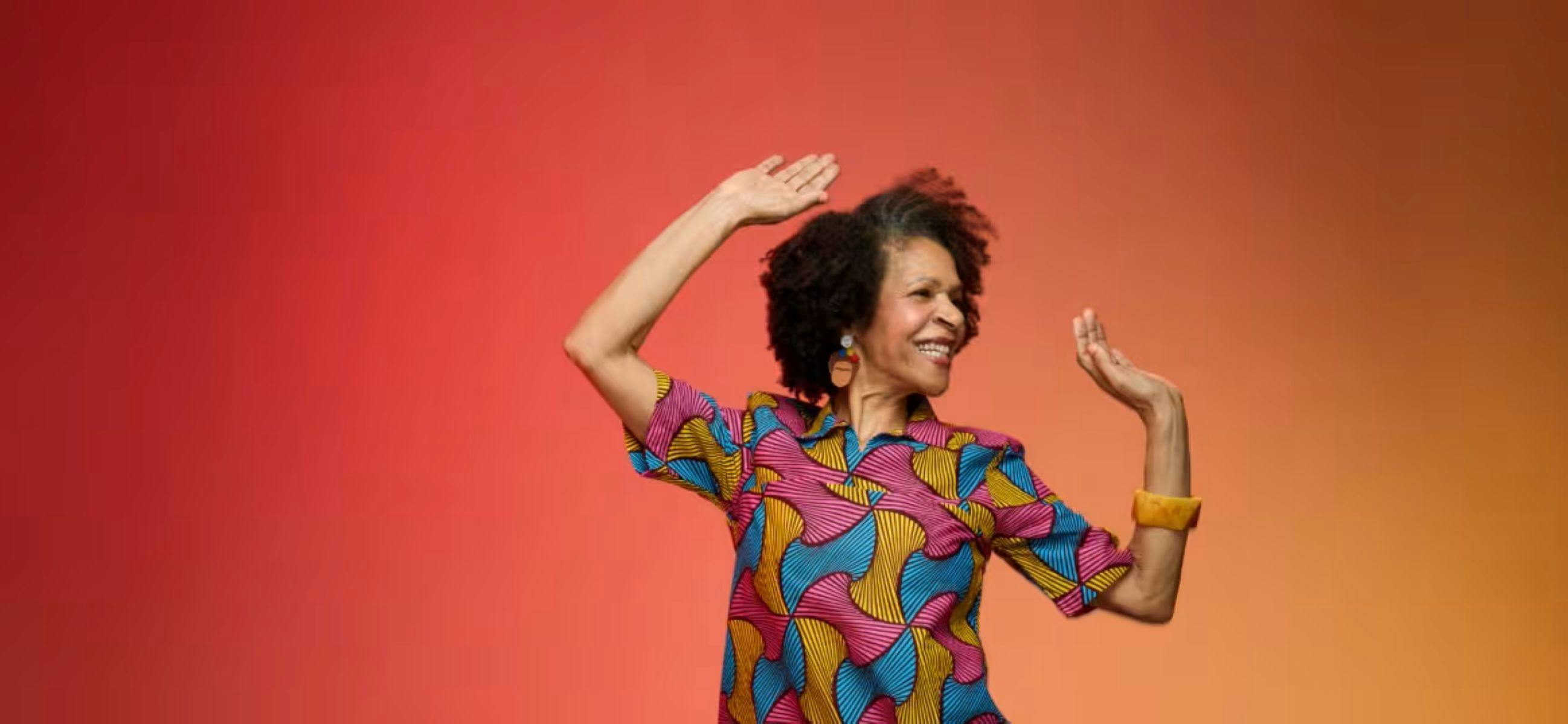 一位黑髮女子身穿色彩鮮豔的連身裙，在橙色的背景下翩翩起舞。