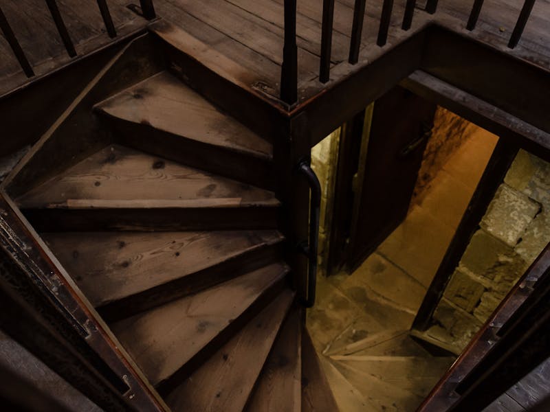 A curving narrow staircase made of dark worn wood with iron railings