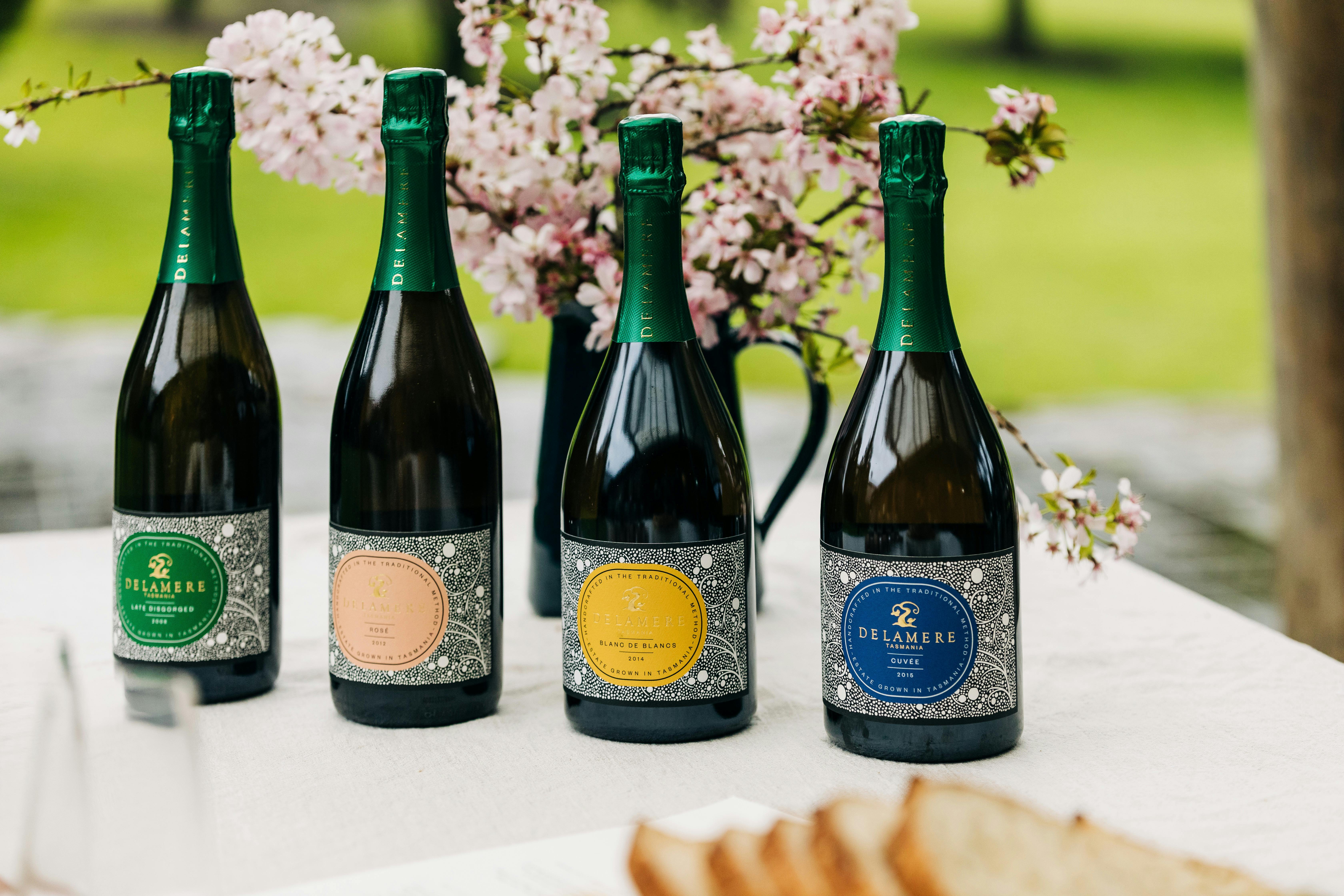 Four bottles of Delamere sparkling wine on picnic table with cherry blossom in the background.