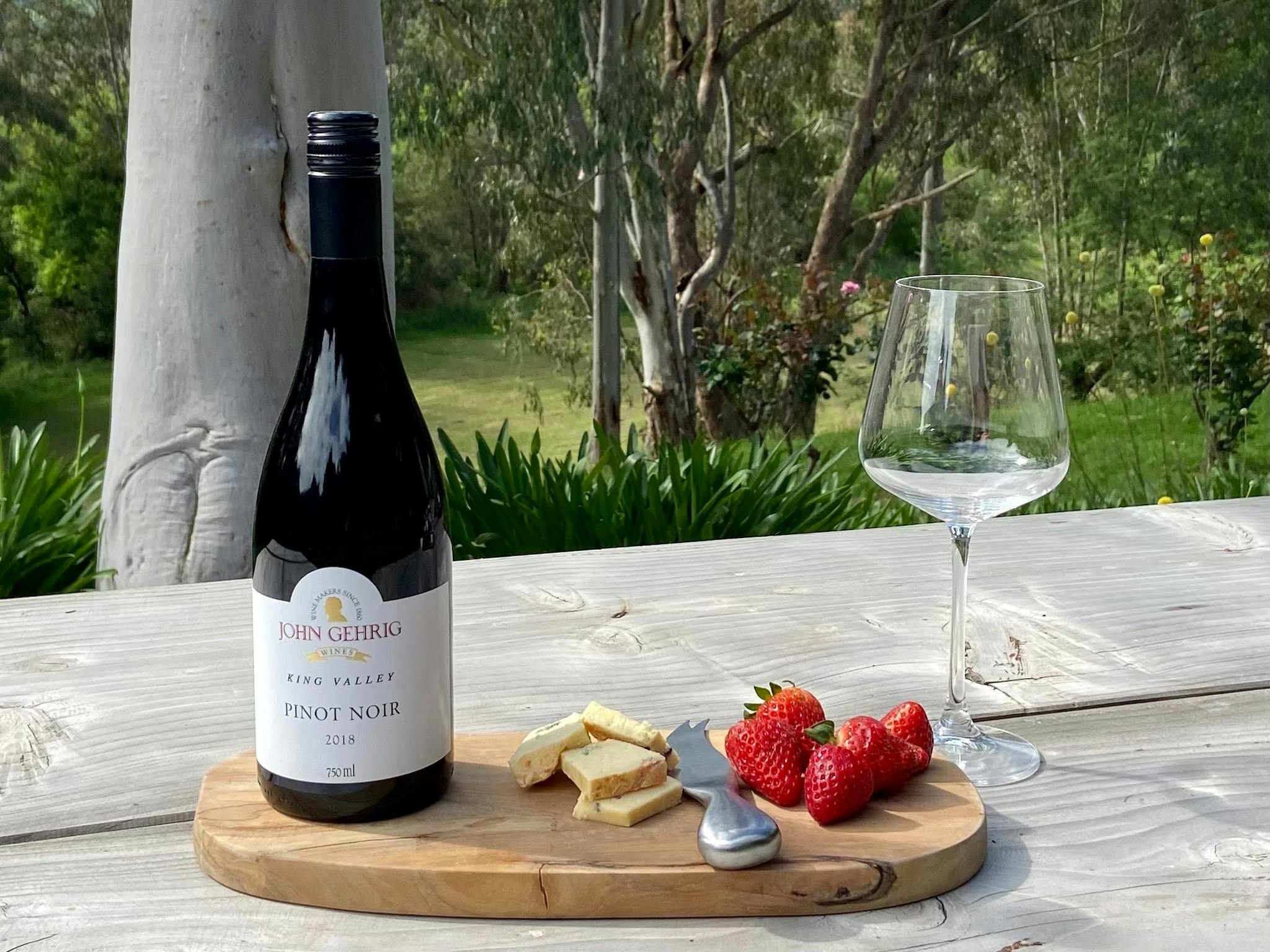 A bottle of King Valley Pinot Noir, outside with some cheese and strawberries.