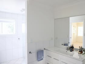 Bathroom with walk in shower, vanity, mirror and white tiled walls.