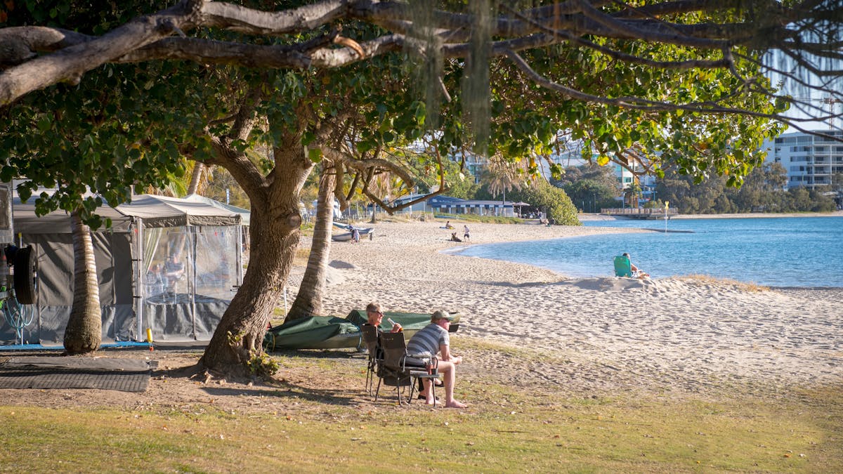 Image of a water front site at Cotton Tree Holiday Park with views of the water and a couple sitting