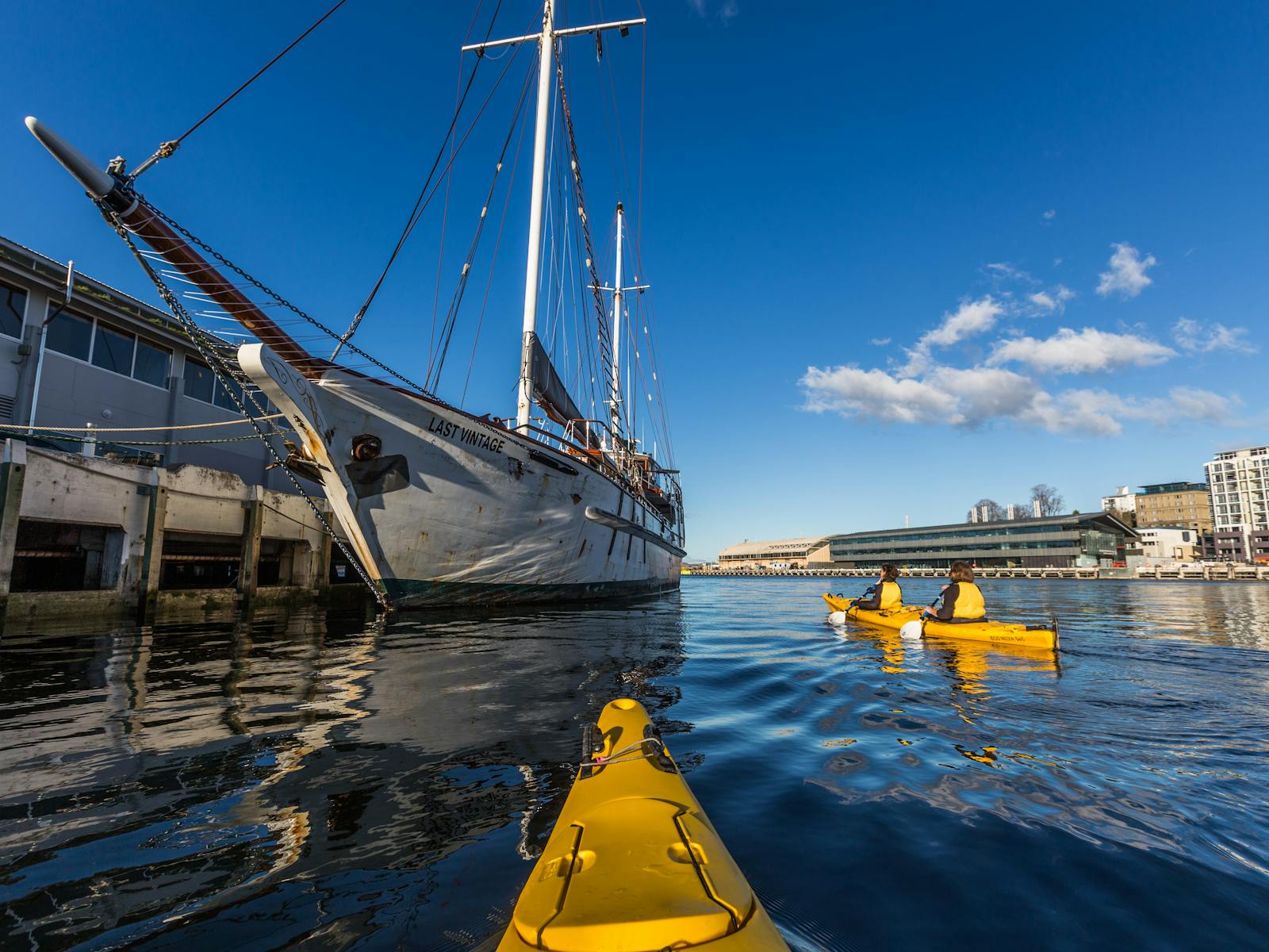 Kayakers paddling beside wooden sailing boat on the Hobart waterfront