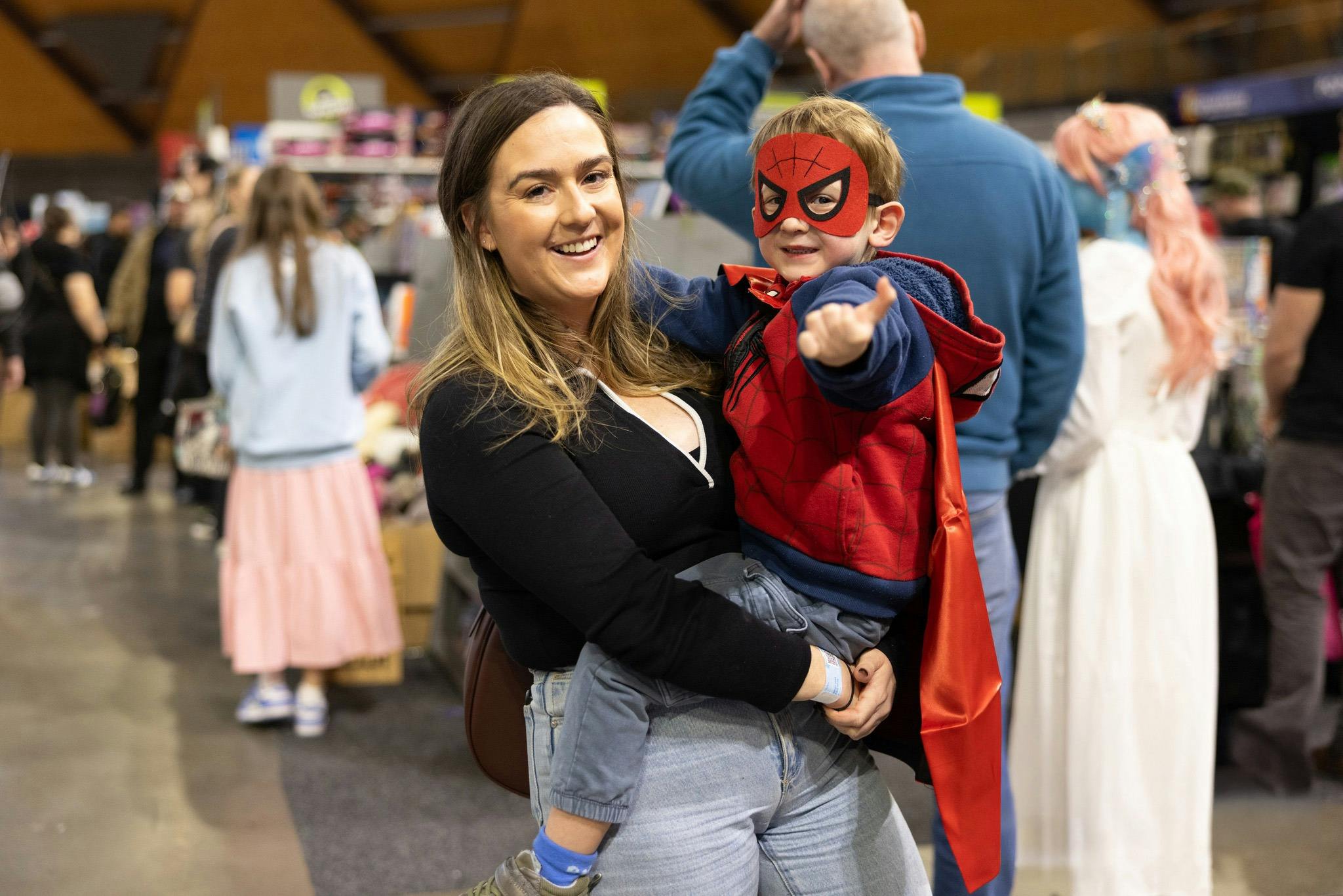 Woman holding child in Spider-Man costume at a Supanova event