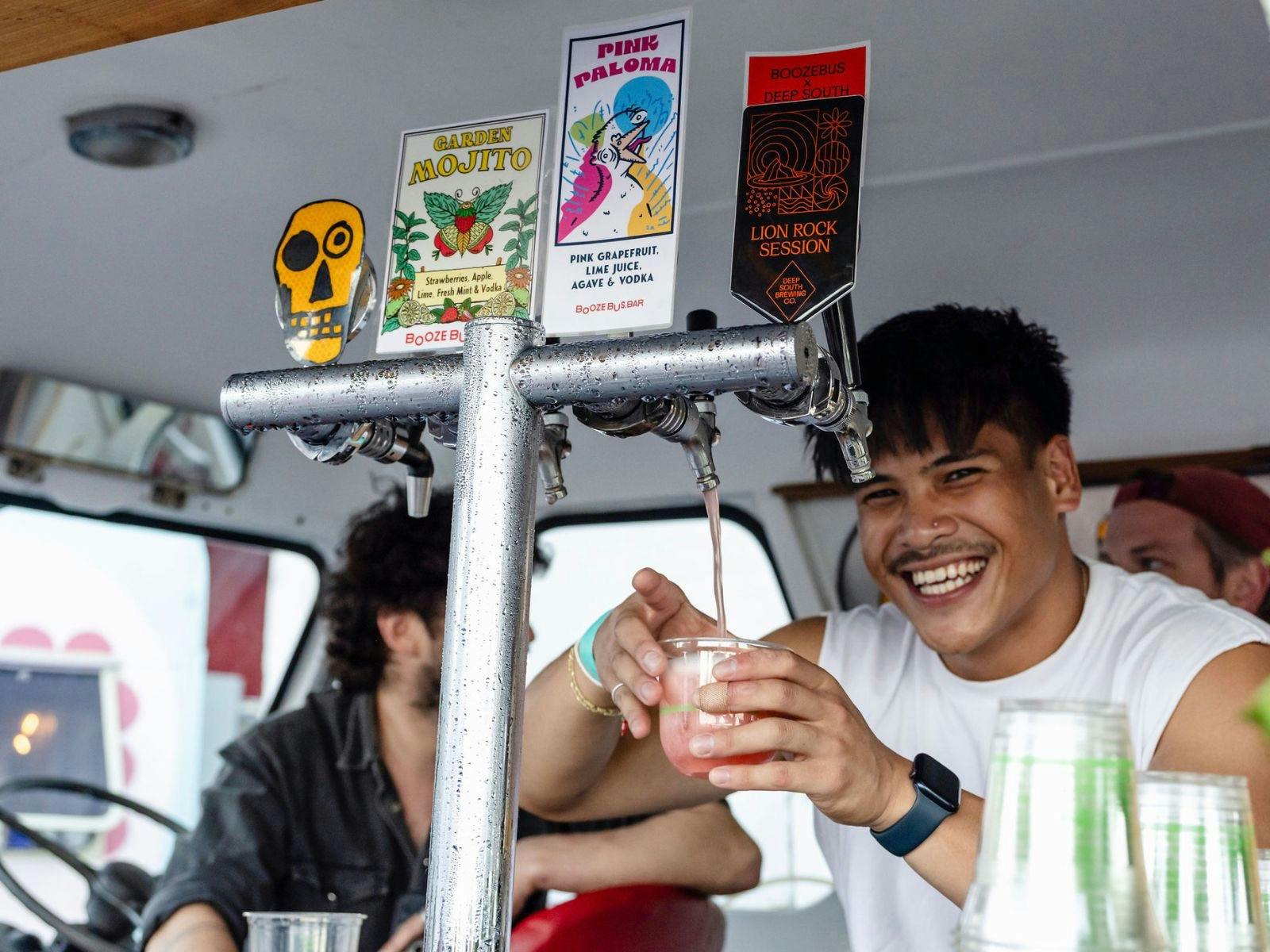 A cheerful man serves drinks from a mini bus converted into a stylish mobile bar.