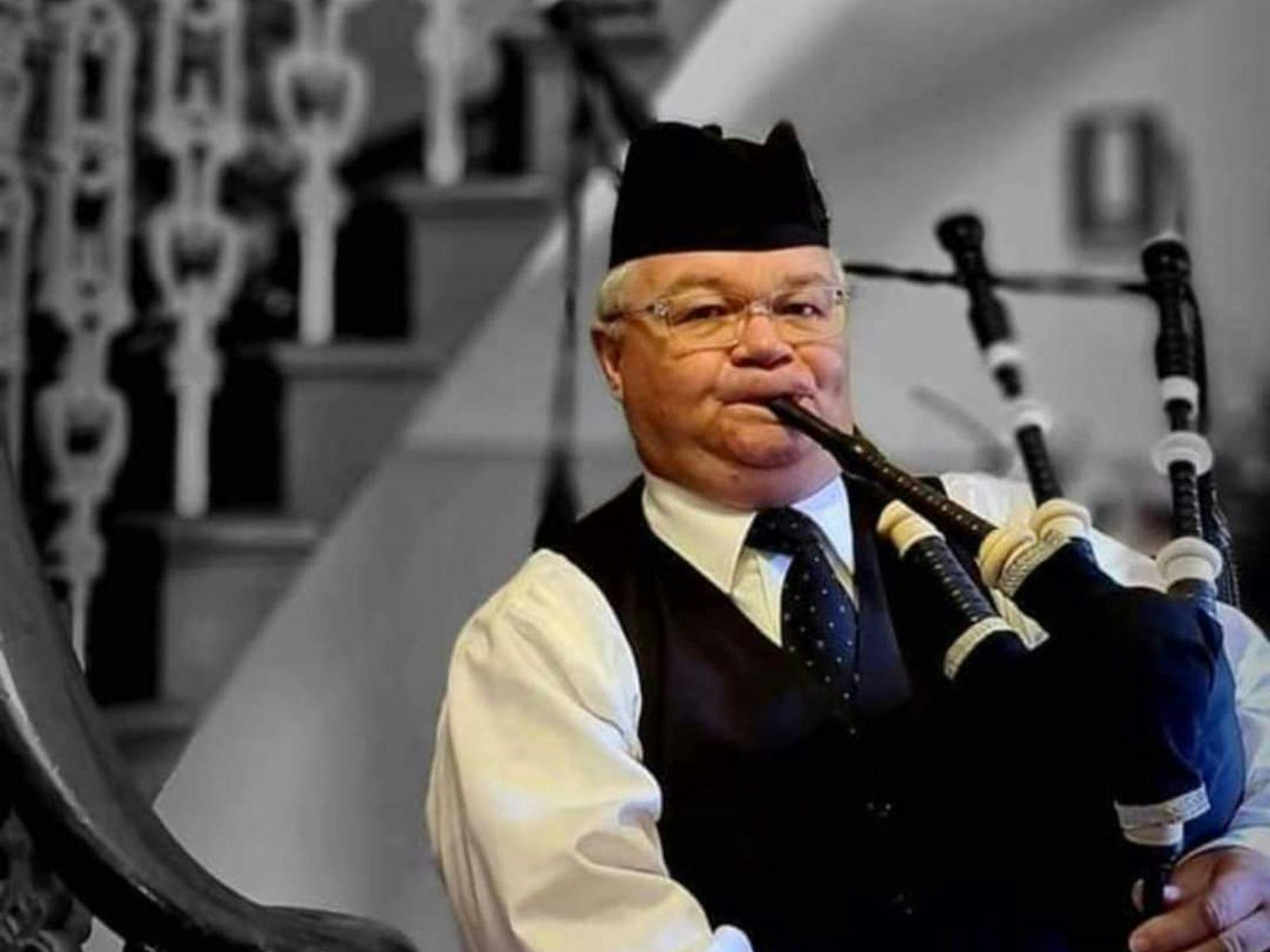 Close up of man playing bagpipes at the base of the stairs, wearing black and white