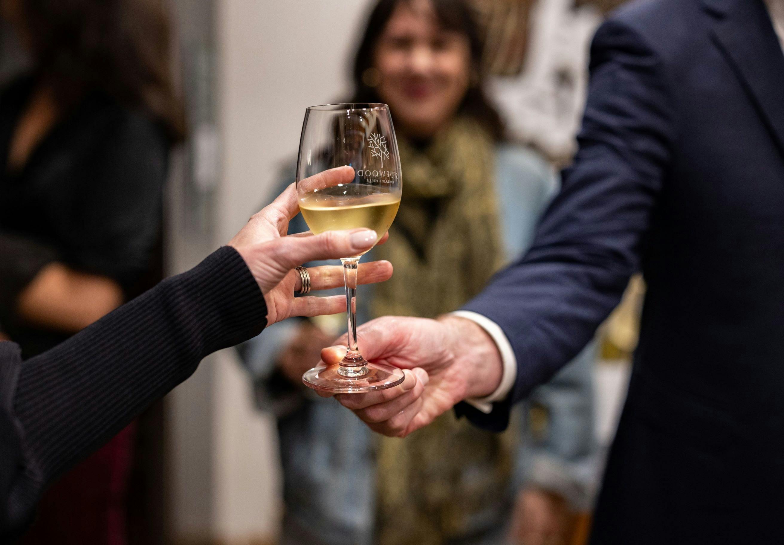 One hand passing a glass of chardonnay to another hand