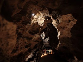 View looking down into Engelbrecht Cave, with rock illuminated and people standing in the distance