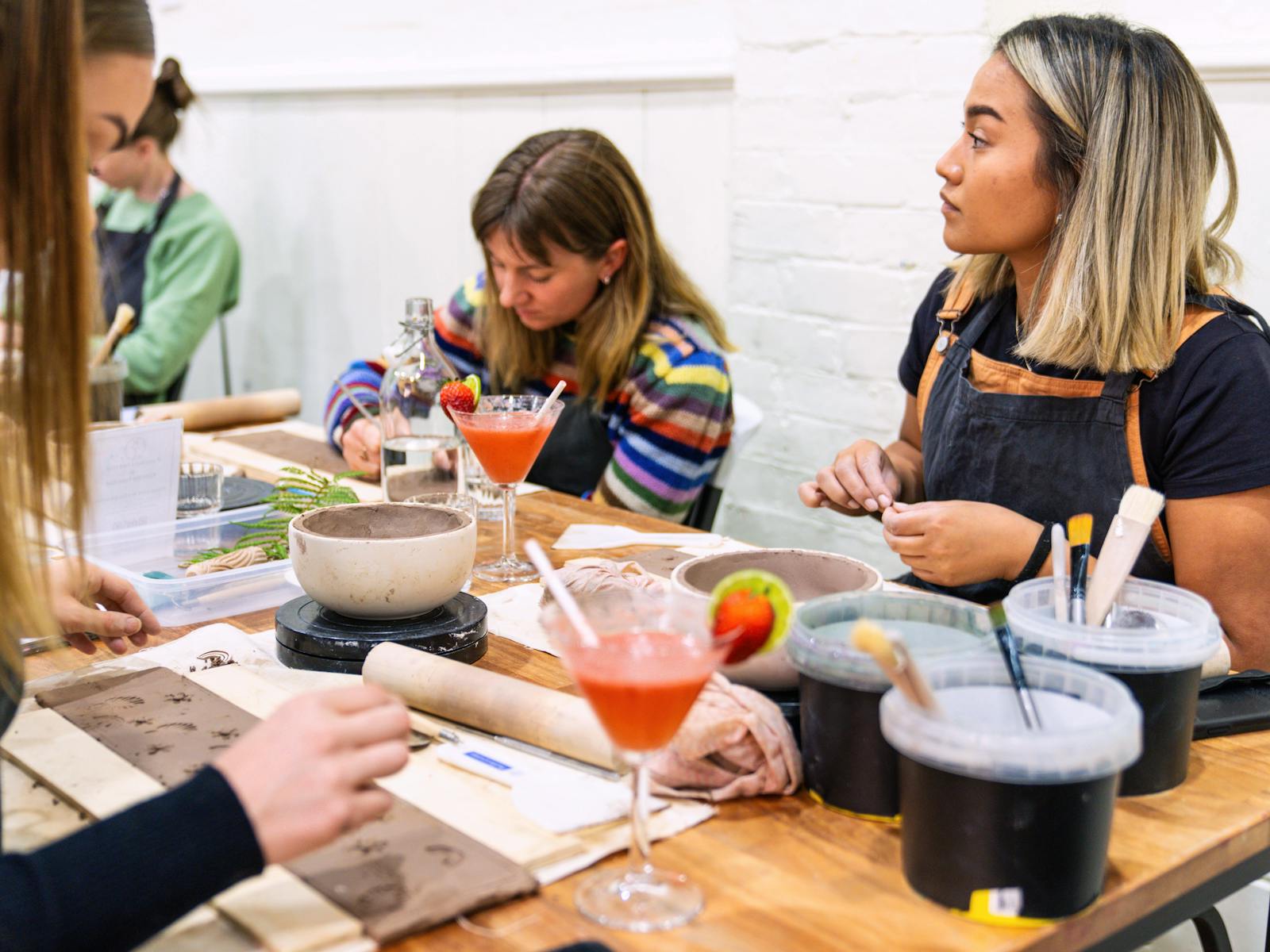 A group hand building pottery with cocktails
