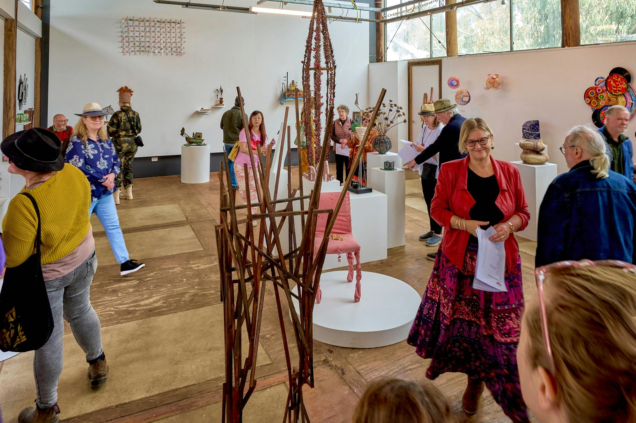 A large steel artwork features in the center of a gallery filled with people.