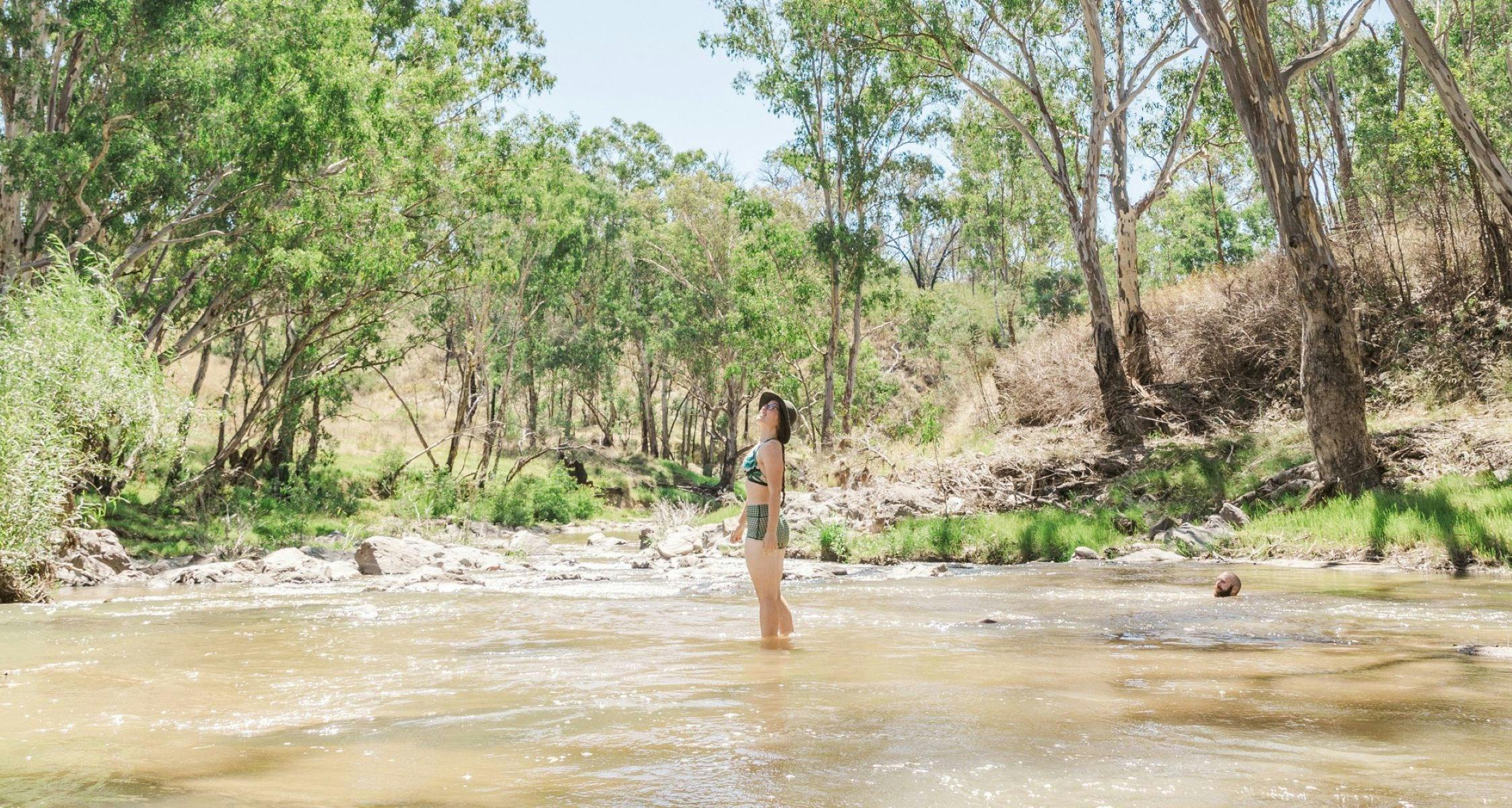 小川に立って、そびえ立つユーカリの木々を見上げている女性。