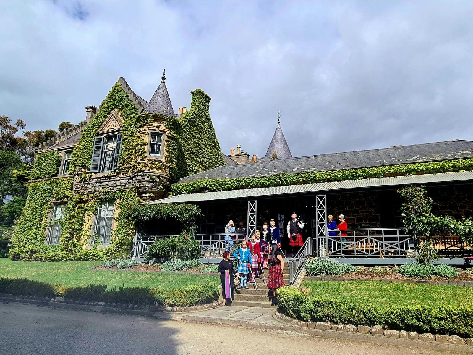 Children and a women stand on the steps of Overnewton Castle,  a grand vine laden homestead