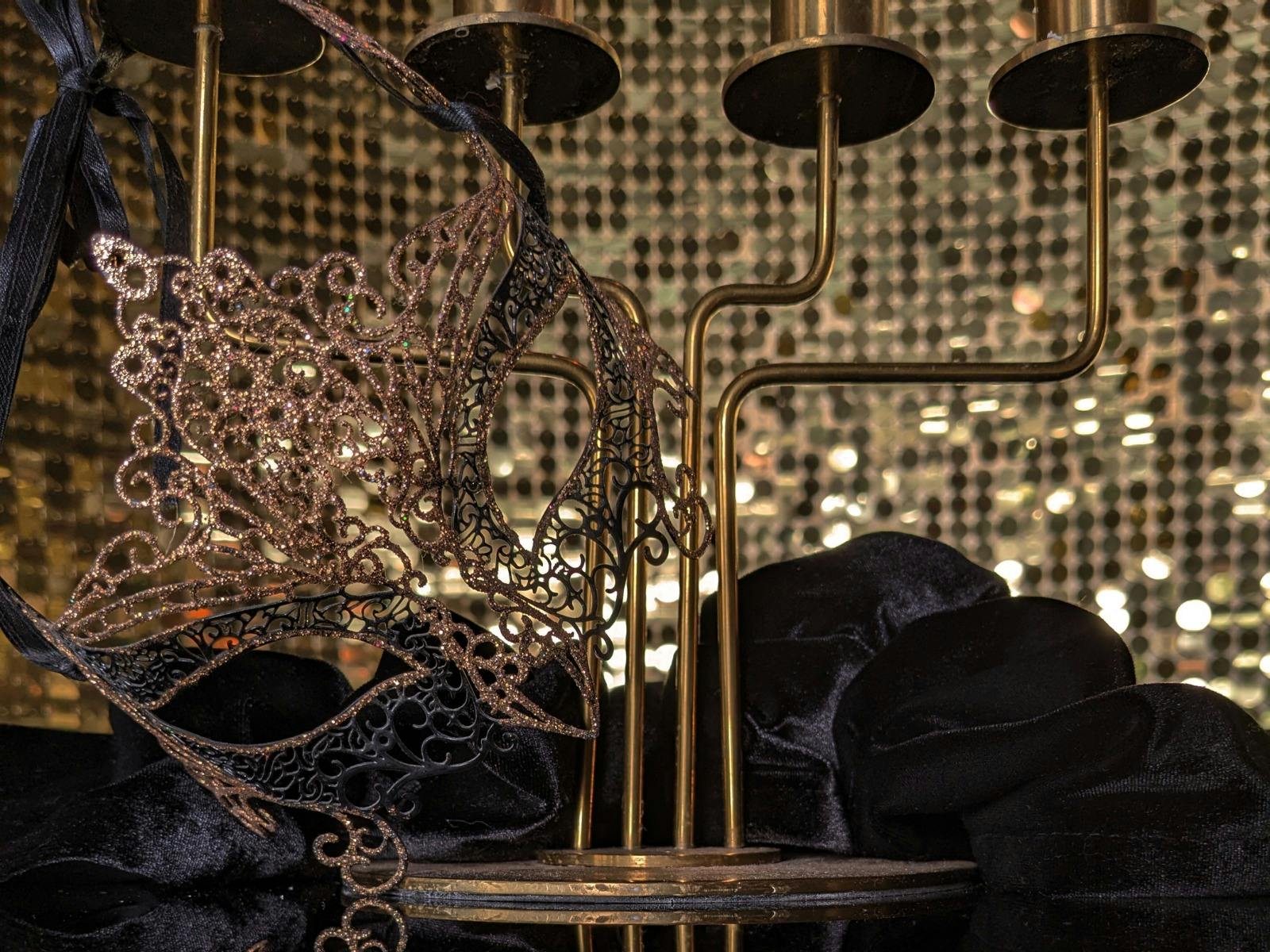 Black and gold mask in front of gold sequin wall