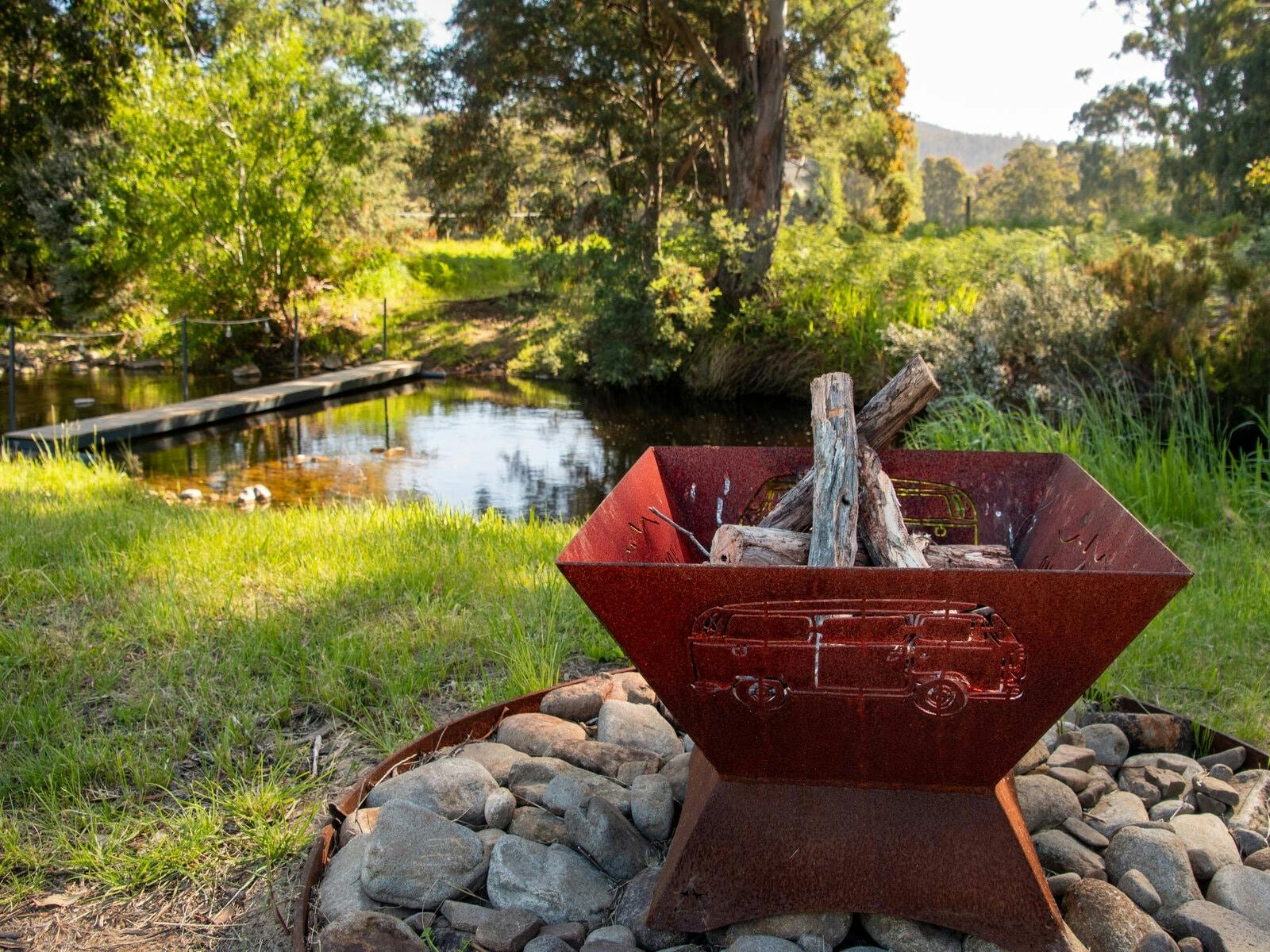 Small open fire pit on a rock base situated near a mountain stream. Small bridge over stream.