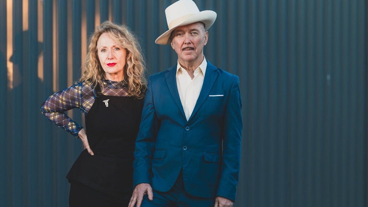 Dave Graney & Clare Moore stand in front of a blue wall