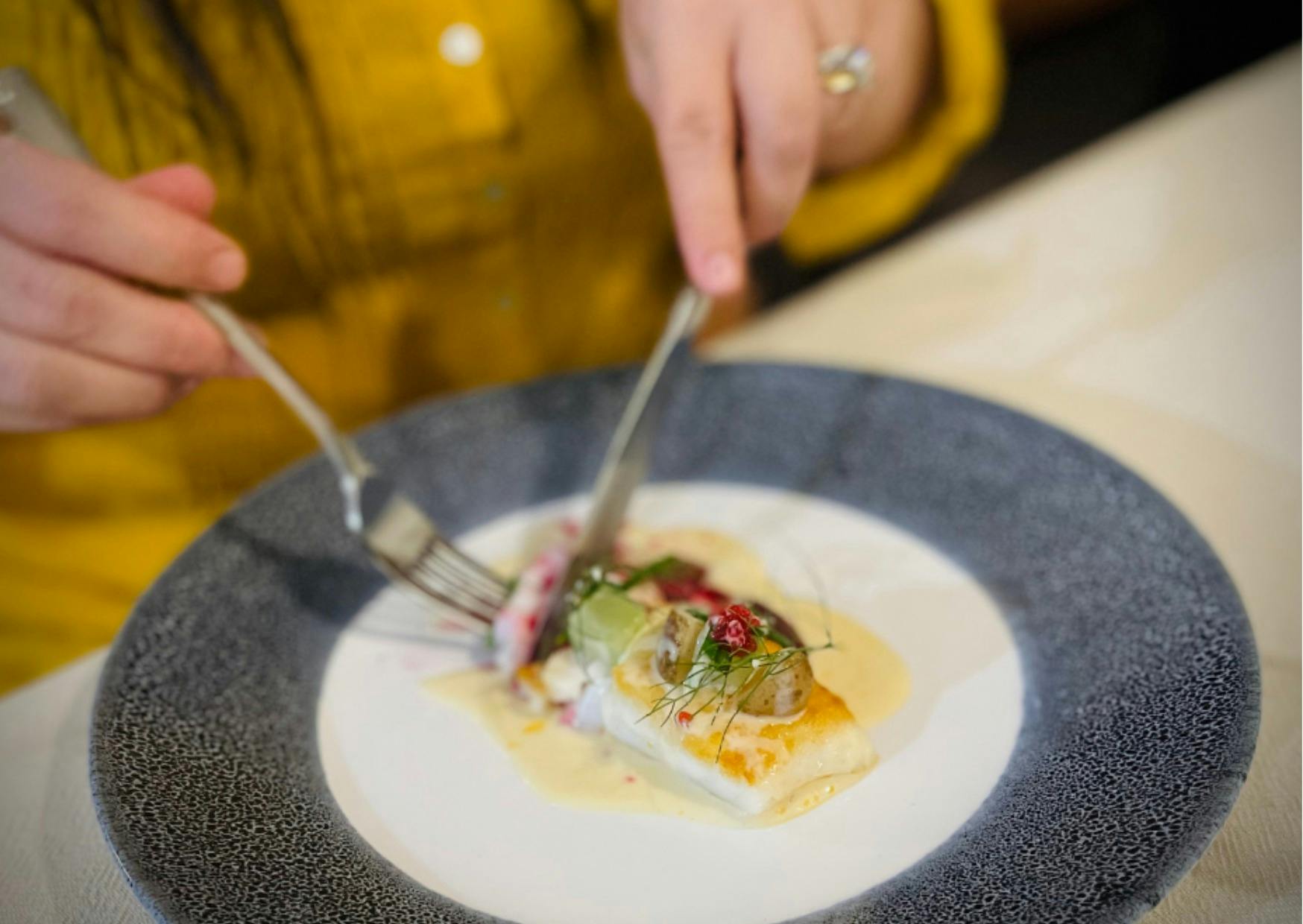 Woman in mustard shirt dines on coral trout dressed with a red claw bisque, fennel, purslane flowers