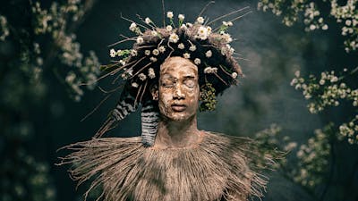 Photograph of a serene young man with eyes closed, with clay body paint, a collar of wild grasses.