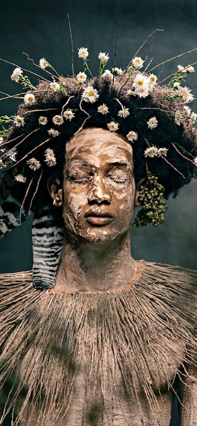 Photograph of a serene young man with eyes closed, with clay body paint, a collar of wild grasses.